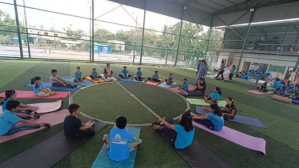 Children practicing yoga together on covered green sports turf